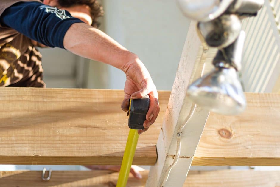 Construction worker holding a measuring tape up to wood rafters