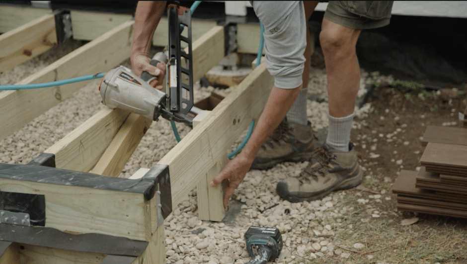 Contractor holds nail gun to beam post on outside deck