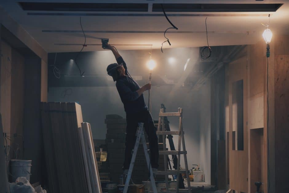 Worker on a ladder reaching towards the ceiling