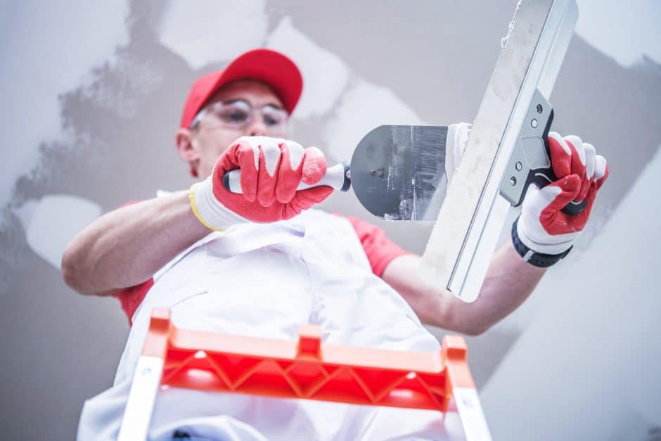 Professional Construction and Remodeling Worker Preparing For Drywall Patching Mixing Joint Compound While Staying on the Ladder.