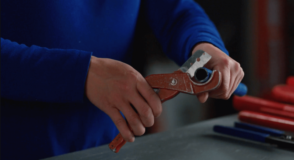 Close-up of pipe cutters gripping a thin blue PEX pipe