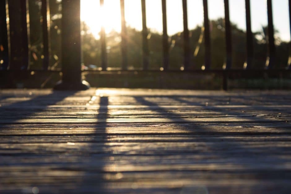 wooden deck with a black fence and sun shining through the beams