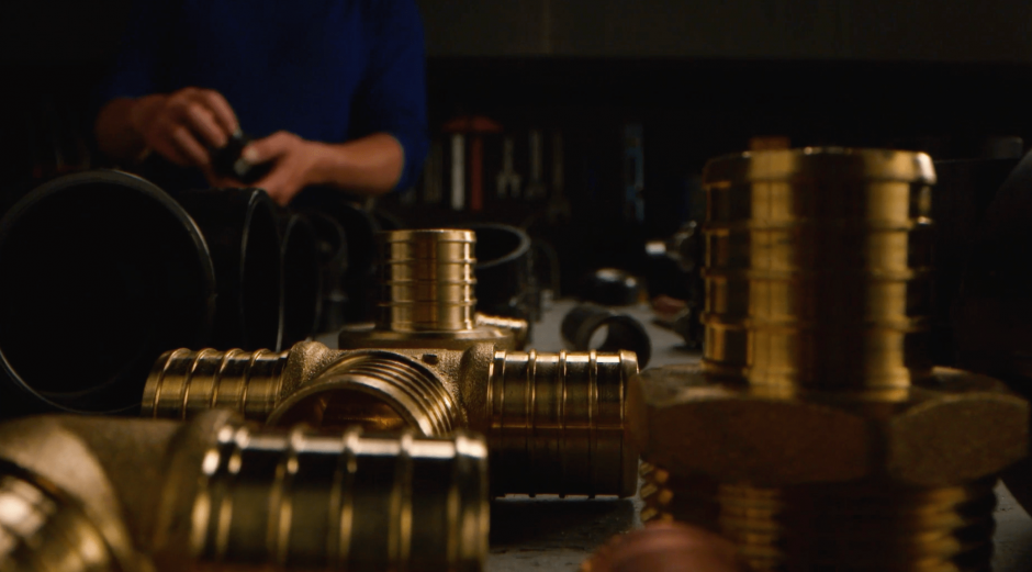 Close-up on pipe fittings with a plumber standing in the background