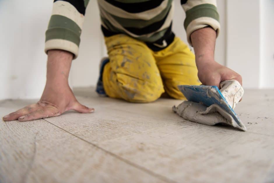 Tilers filling the space between ceramic wood effect tiles using a rubber trowel on the floor in new modern apartment