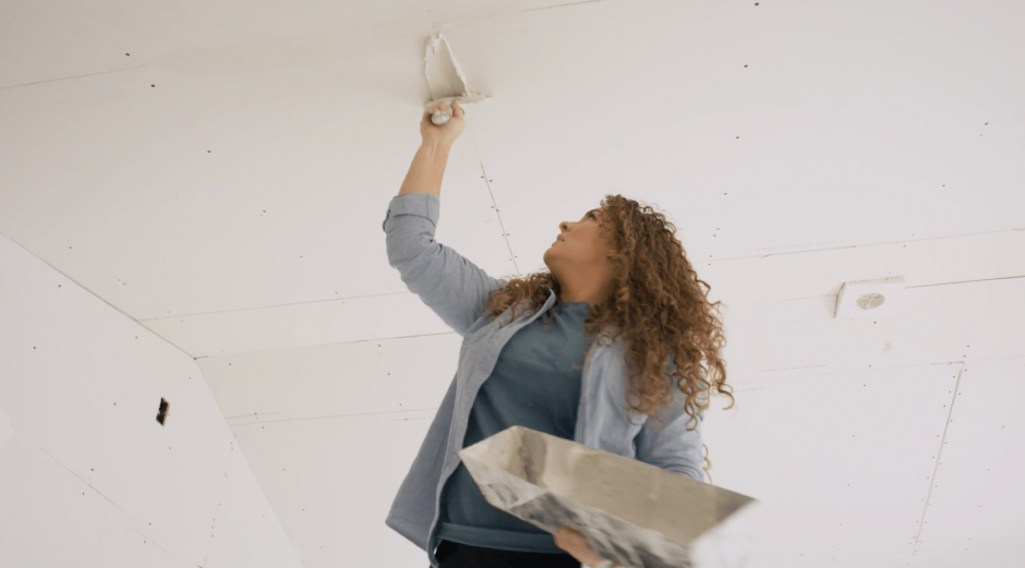 Drywall contractor stands on a ladder fixing an uneven drywall board