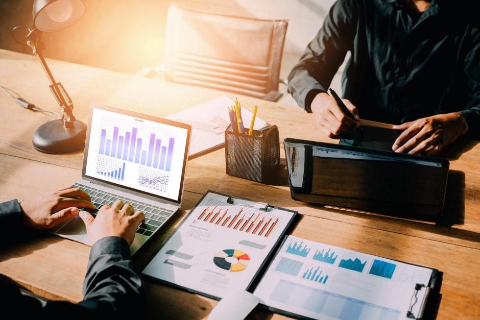 Working on computers with charts and graphs across the desk