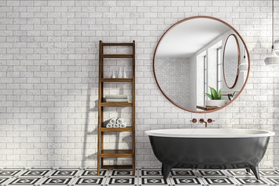 Minimalistic bathroom interior with brick walls, tiled floor, black bathtub with round mirror hanging above it