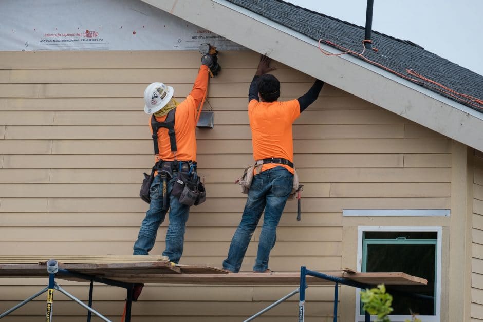 Construction workers installing vinyl siding facade on scaffolding system