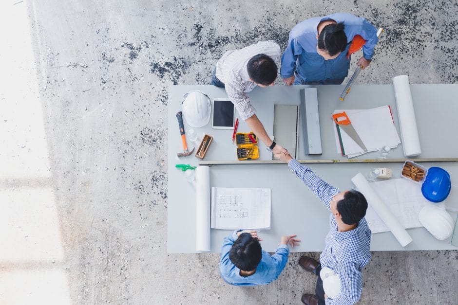 Construction team reviews blueprints on a table and shakes hands